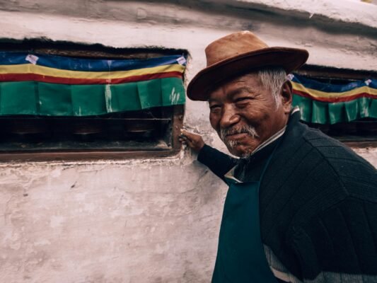 Charming portrait of an elderly man with a friendly smile, near prayer wheels.