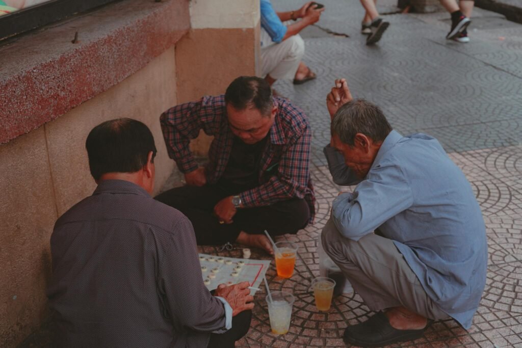Three elderly men engaged in a board game on a sidewalk in Ho Chi Minh City.