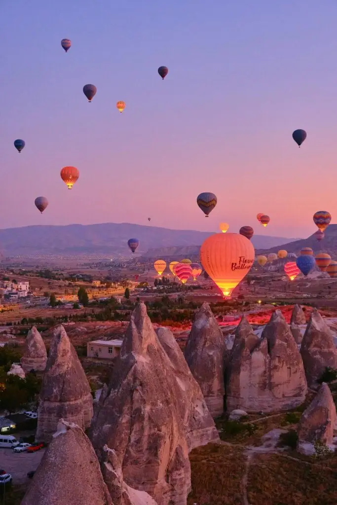 Vibrant hot air balloons float over Cappadocia's stunning rock formations at sunset.