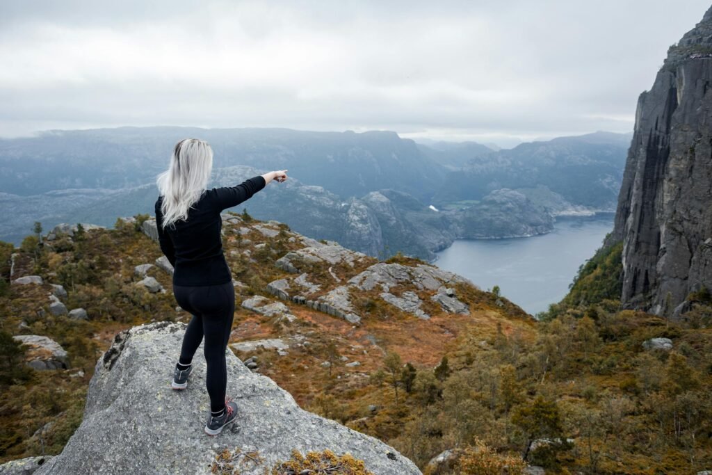 A woman on a hiking adventure pointing towards a stunning fjord in Norway.